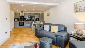 Uma sala de estar moderna com um sofá cinza, uma mesa de centro e uma área de jantar ao fundo.
