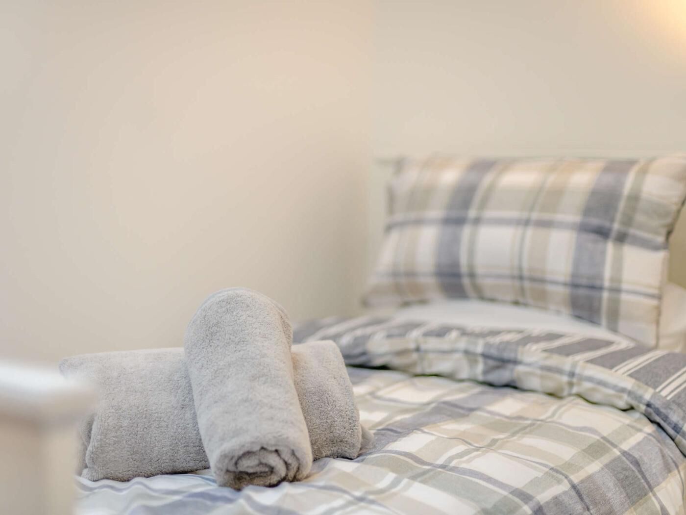 Un letto con biancheria a quadri e asciugamani arrotolati.