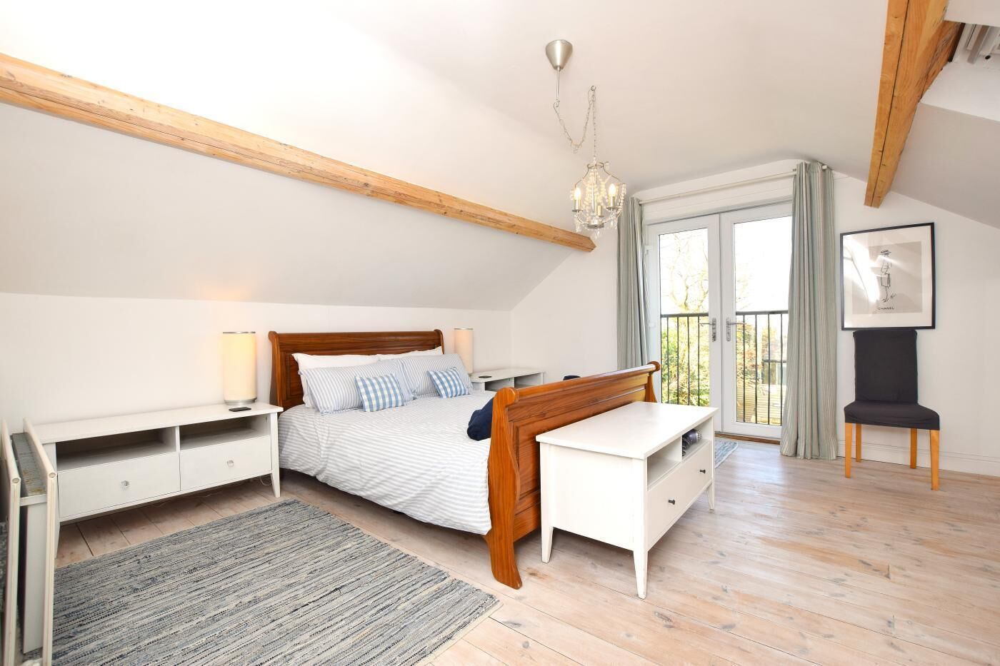 A bedroom with a bed, bedside tables, a desk, a chair, a chandelier, and a balcony with curtains.