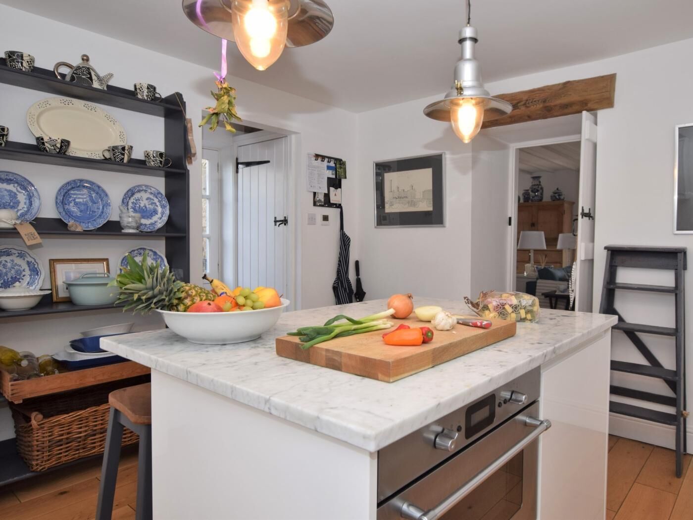 A kitchen with a marble countertop, a fruit bowl, a cutting board with vegetables, and hanging pendant lights.