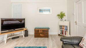 Una sala de estar con televisor, estantería, un cofre de madera y una puerta.