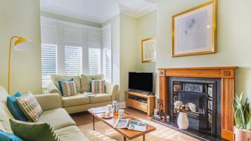 A living room with a sofa, coffee table, fireplace, television, and a framed picture on the wall.