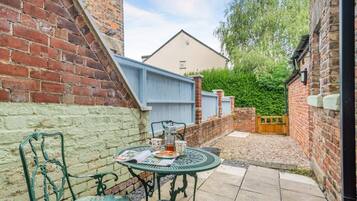 A patio with a table and chairs, a brick wall, a blue fence, and a hedge in the background.