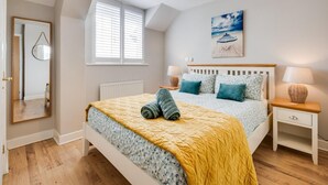 Quarto com cama, duas mesas de cabeceira, luminária pendente, janela com persianas, um quadro e um espelho.