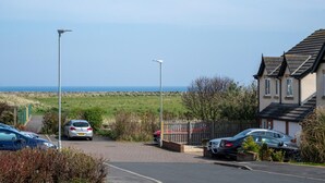 Uma área de estacionamento com carros, um edifício com telhado inclinado e vista para o mar.