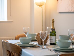 Een eettafel gedekt met borden, kommen, bestek en een fles wijn.