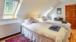 A bedroom with two beds, a window, a radiator, a wooden door, and a small table with a vase. - 3 Bed in Perth (oc-50031) (Stanley)