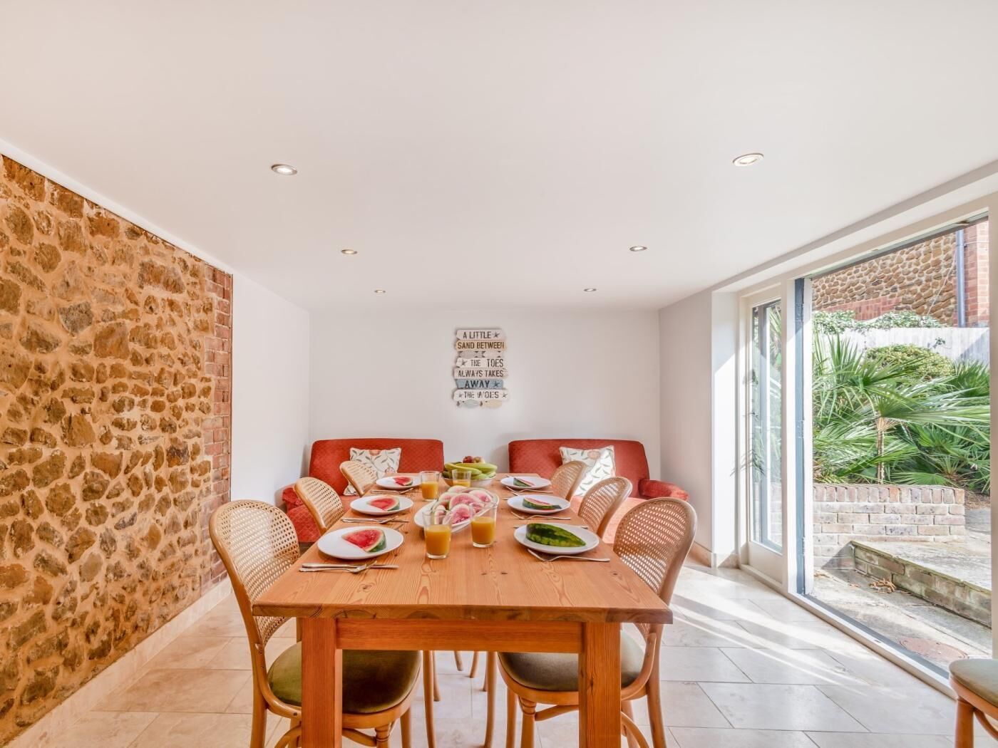 Un coin repas agrémenté d’un mur en pierre, d’une table en bois dressée pour quatre personnes et offrant une vue sur l’extérieur.