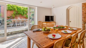 Un coin repas avec une table dressée pour quatre personnes, un téléviseur et une vue sur un jardin, visible à travers une porte vitrée.