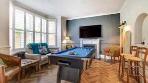 Une table de billard dans un salon, avec un téléviseur au-dessus, une cheminée et un coin bar avec des chaises.