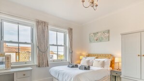 Une chambre à coucher comprenant un lit, des tables de chevet, un bureau, une armoire et une fenêtre avec des rideaux.