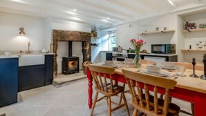 A modern kitchen with a built-in wood stove, a dining area with wooden chairs, and a kitchen island with a sink and a kettle. - 2 Bed in Hope Valley (oc-88979) (Sheffield)