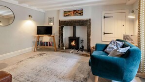 A living room with a fireplace, a television on a stand, a bookshelf, and a teal armchair. - 2 Bed in Hope Valley (oc-88979) (Sheffield)