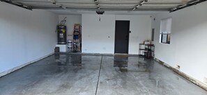 Eine saubere, leere Garage mit Betonboden, einer schwarzen Tür und einem Fenster mit Rollläden.