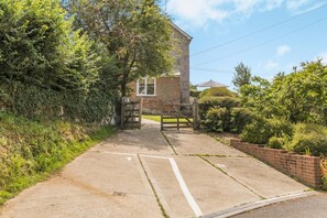 A gated entrance to a property with a paved driveway leading to a brick building. - 3 Bed in Ventnor (oc-ic179) (Godshill)