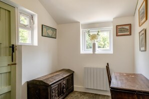 A room with a wooden bench, a radiator, a window with a vase of flowers, and framed pictures on the wall. - 3 Bed in Ventnor (oc-ic179) (Godshill)