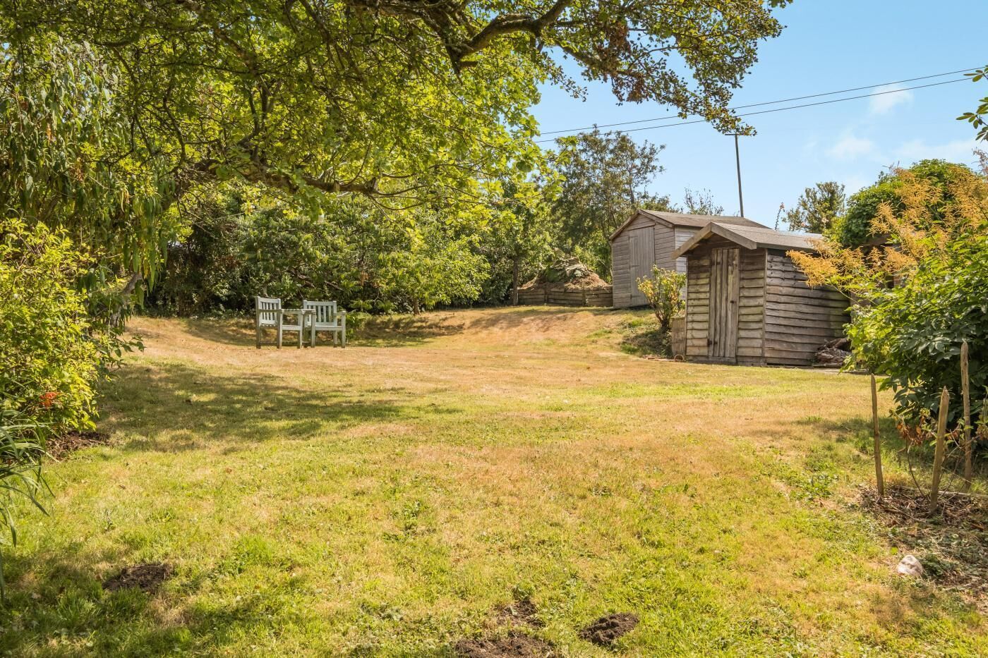 Une cour gazonnée avec un abri en bois et deux chaises en bois.