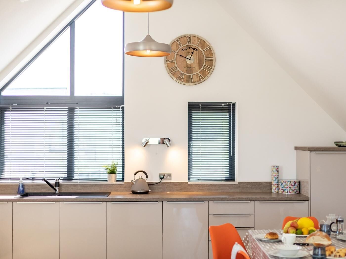 Eine moderne Küche mit Oberlicht, einer Holz-Uhr und einem Essbereich mit gedecktem Frühstückstisch.