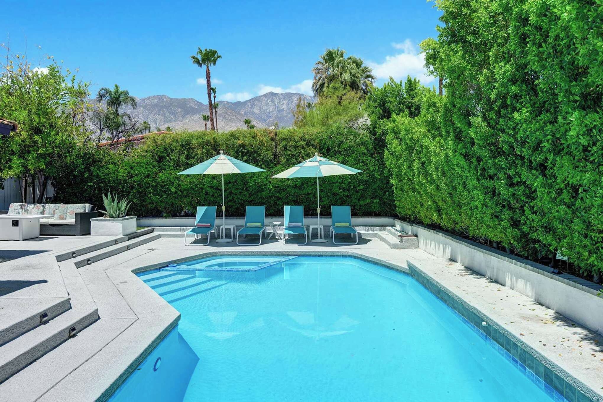 The property's outdoor pool area offers lounge seating surrounded by mature landscaping, with mountain ranges visible in the background.