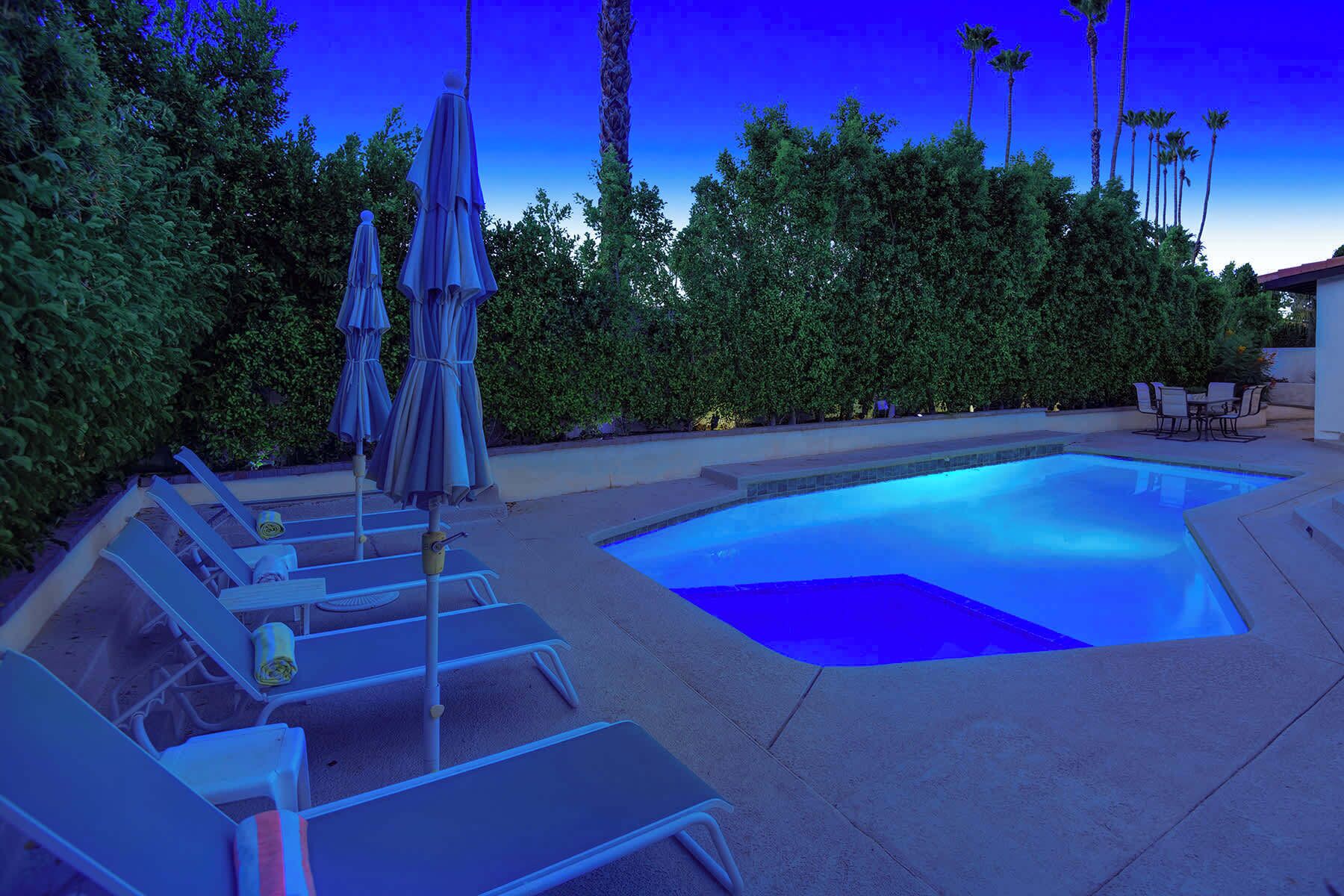 A swimming pool with lounge chairs and umbrellas, surrounded by greenery and palm trees.