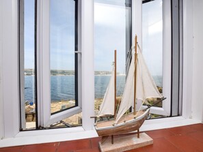 Ein Modellsegelboot in einem Fenster mit Blick auf das Meer und eine ferne Küste.