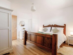 Ein Schlafzimmer mit einem hölzernen Bett, weißen Wänden, einem Holzschrank, einem Spiegel und einer weißen Lampe.