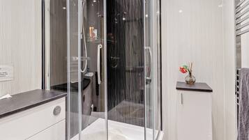 A modern bathroom with a glass-enclosed shower, a vanity with a dark countertop, and a small shelf with a vase.
