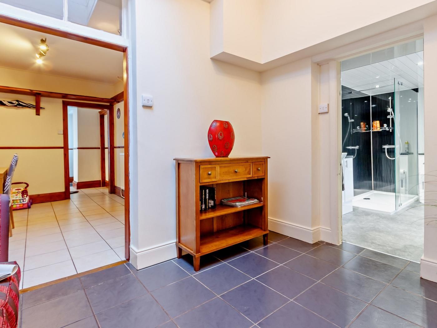A modern interior with a wooden console table, a red vase, and a glass shower enclosure.