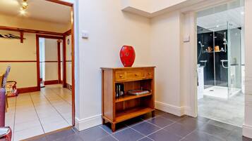 A modern interior with a wooden console table, a red vase, and a glass shower enclosure.