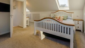A bedroom with a sloped ceiling, a skylight, a white bed with a wooden headboard, a bedside table, and a wardrobe. - 4 Bed in Freshwater (oc-91115) (Freshwater)