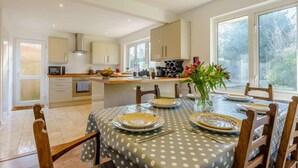 A modern kitchen with a dining area, featuring a central island, a large window, and a view of the outdoors. - 4 Bed in Freshwater (oc-91115) (Freshwater)