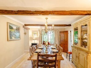 Un comedor con una mesa de madera dispuesta para seis personas, flanqueada por sillas, una araña y un aparador con puertas de cristal.