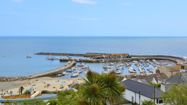 Un pueblo costero con un puerto deportivo, una playa de arena y edificios a lo largo del frente marítimo.