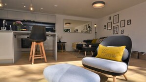 Una sala moderna con sofá, reposapiés y comedor, con una cocina al fondo.
