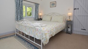 Quarto com cama, janela com cortinas, mesa de cabeceira com abajur e porta.