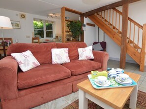 A cozy living room with a red sofa, a wooden staircase, and a dining area in the background. - 1 Bed in Bridport (oc-dc113) (West Milton)