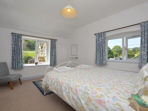Ein Schlafzimmer mit Bett, Stuhl, Fenster und einer Pendelleuchte.