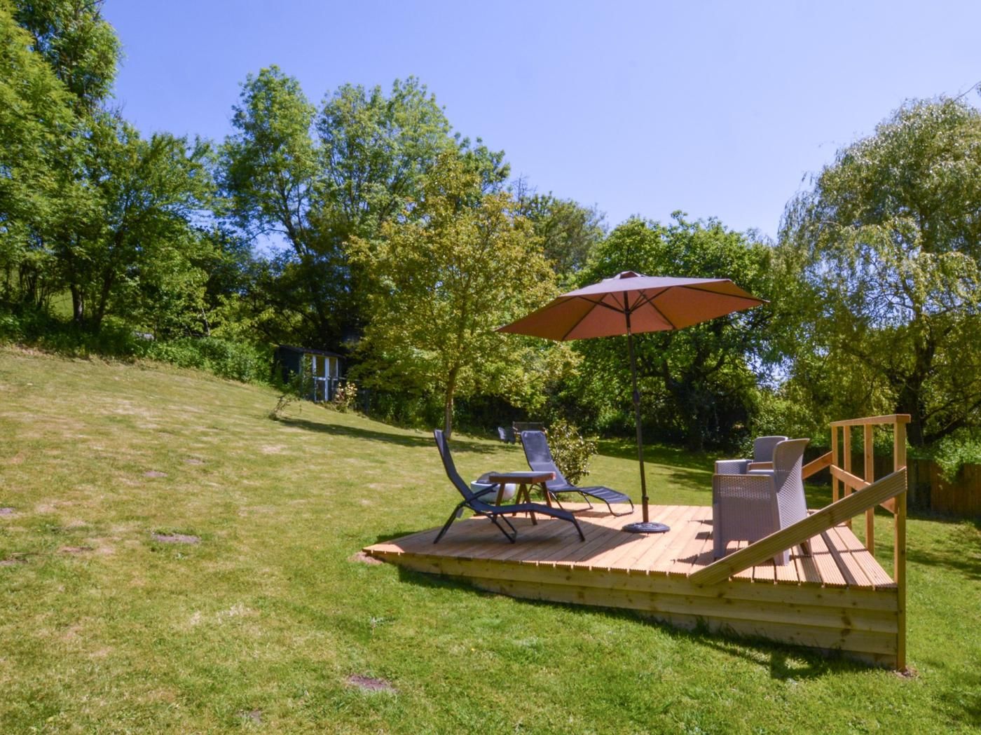 A wooden deck with outdoor furniture, including two chairs and a table, under a large umbrella.