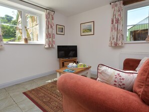 Ein gemütliches Zimmer mit Fernseher, einem kleinen Tisch mit Tassen und Untertassen, einer Couch und einem Fenster mit Vorhängen.