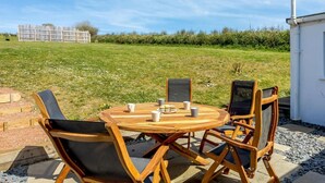 Ein Holztisch mit Stühlen in einer Außenanlage, mit einem grasbewachsen Feld und einem weißen Gebäude im Hintergrund.