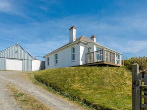 Una casa de dos pisos con fachada blanca, un deck de madera y un camino de entrada de grava.
