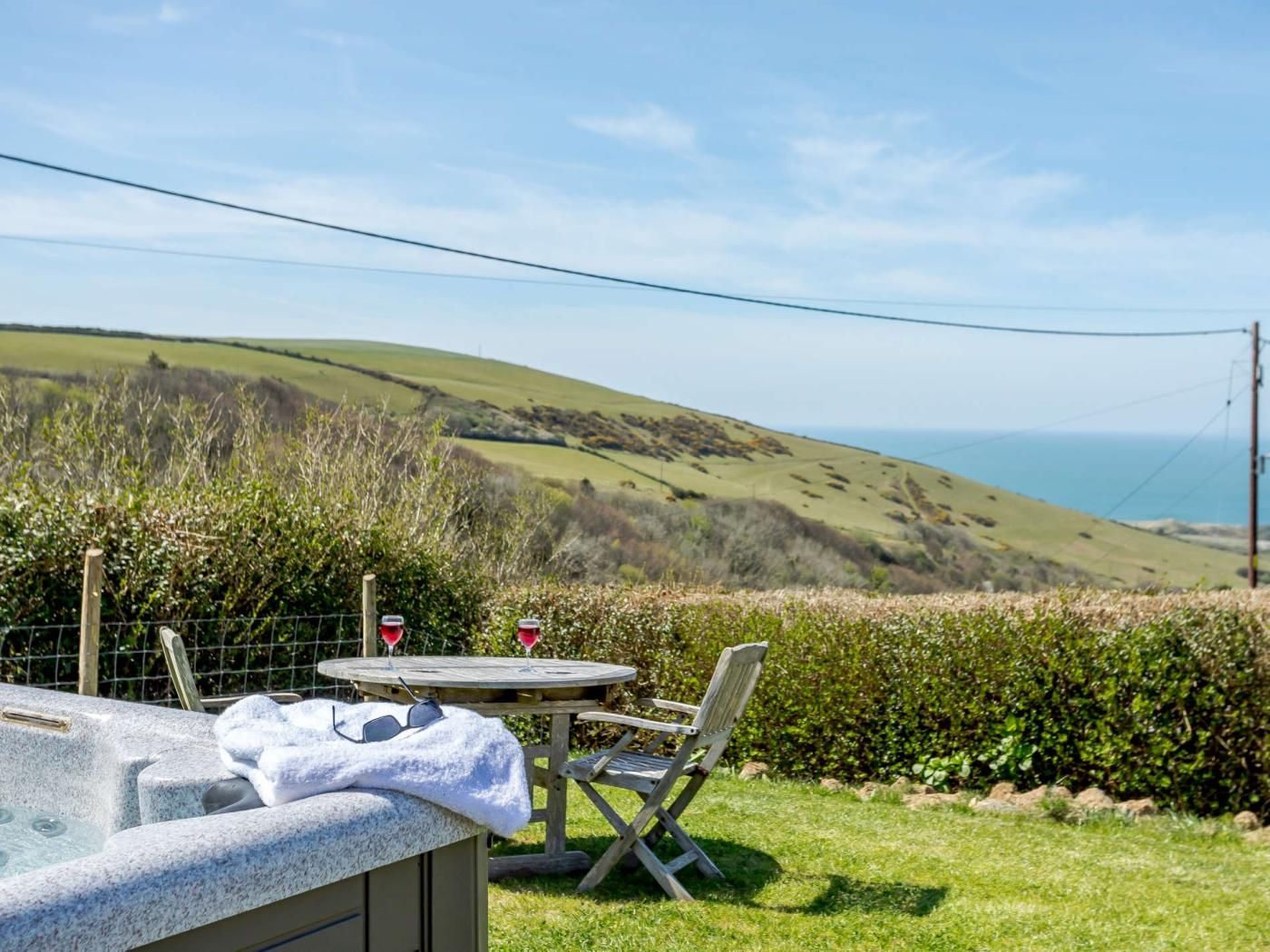 A hot tub with a table and chair, a view of rolling hills, and a body of water in the distance.