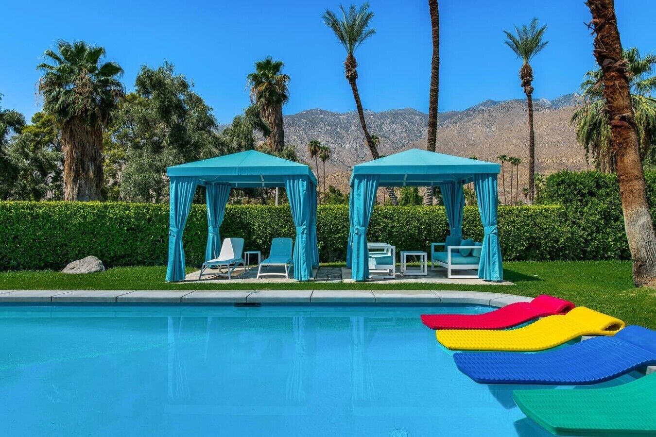 A pool area with two gazebos, lounge chairs, and a clear view of mountains in the background.