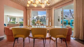 A dining area with a glass table, three chairs, and a chandelier. - 4,775 Sq Ft MidMod Estate, 5 King Beds, All En Suites, Saltwater Pool, Spa (Palm Springs)