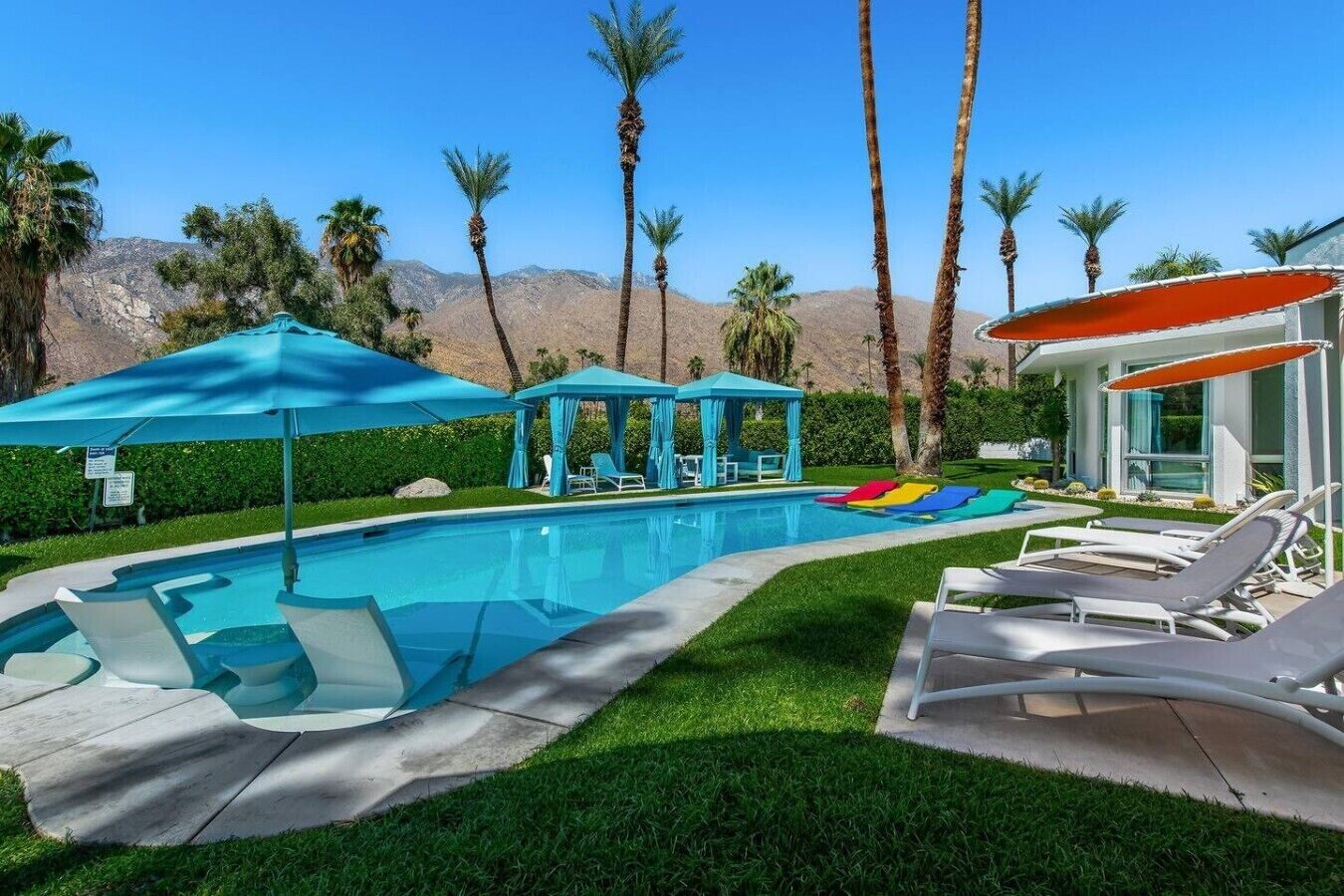 A swimming pool with lounge chairs, a cabana, and palm trees.