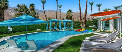 A swimming pool with lounge chairs, a cabana, and palm trees.