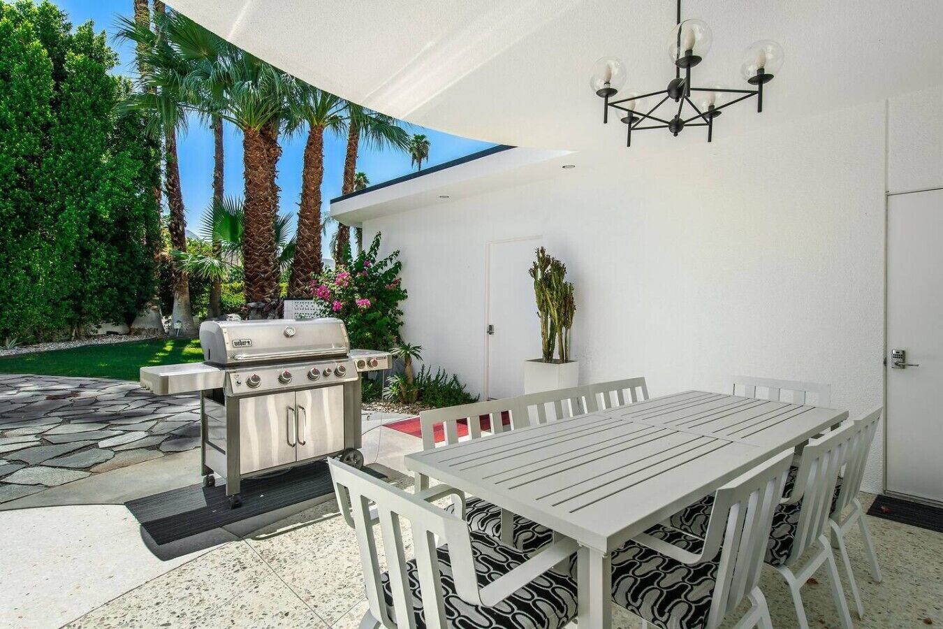 An outdoor patio with a grill, white table, chairs, and a ceiling light fixture.