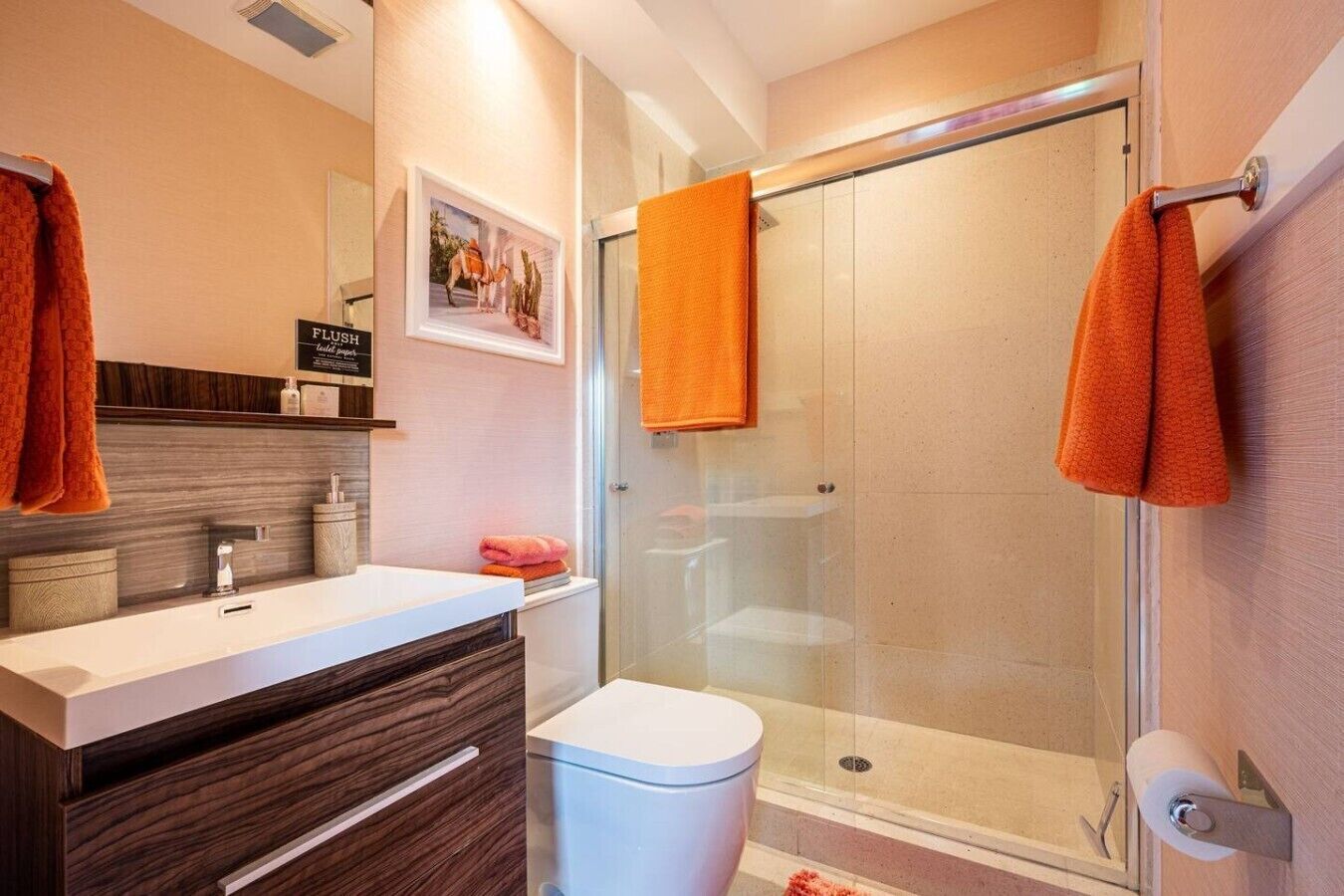 A modern bathroom with a glass shower enclosure, a white sink, and dark wood cabinetry.