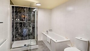 Un baño moderno con ducha de vidrio, bañera independiente y retrete.
