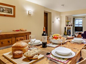 A dining table set with bread, wine, and fruit, in a room with a wooden cabinet and a painting on the wall. - 2 Bed in Skipton (oc-94261) (Airton)